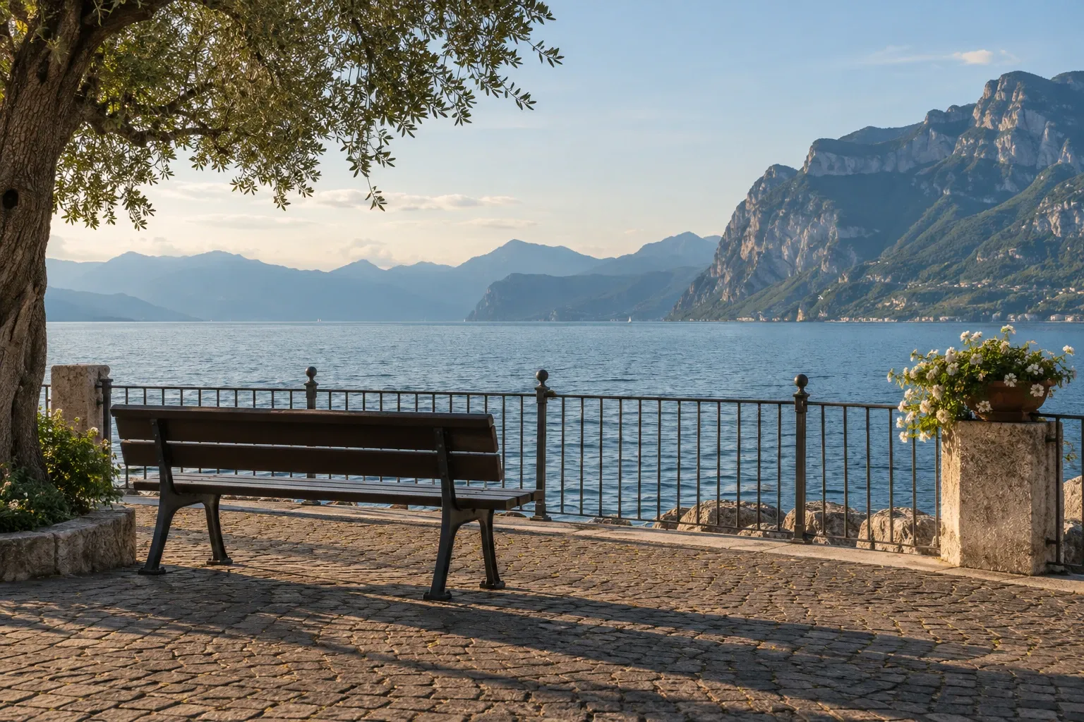 Panchina vuota sul lungolago con vista sul Lago di Garda e montagne sullo sfondo